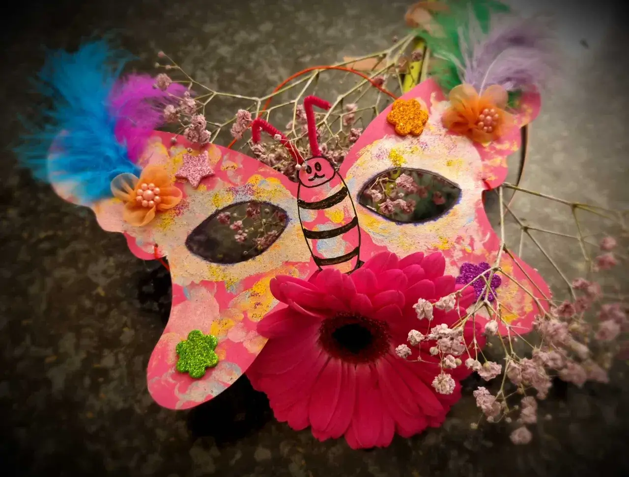 Bunte Schmetterlings-Faschingsmaske mit Federn, Blumen und Glitzer. Eine Vorlage zum Basteln f&uuml;r Karneval.