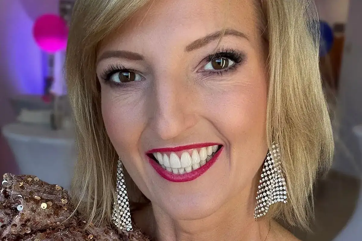 Uśmiechnięta kobieta w cekinowej sukience i błyszczących kolczykach. To cała prawda o jej makijażu Mary Kay.