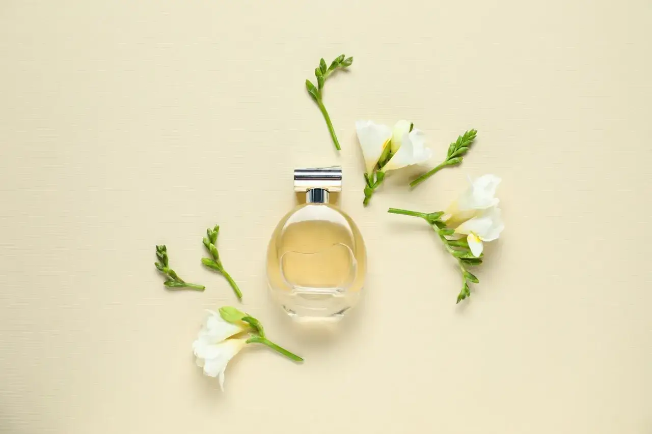 Elegancka butelka perfum otoczona delikatnymi kwiatami frezji. Ich subtelny zapach unosi się w powietrzu, tworząc atmosferę luksusu i świeżości.