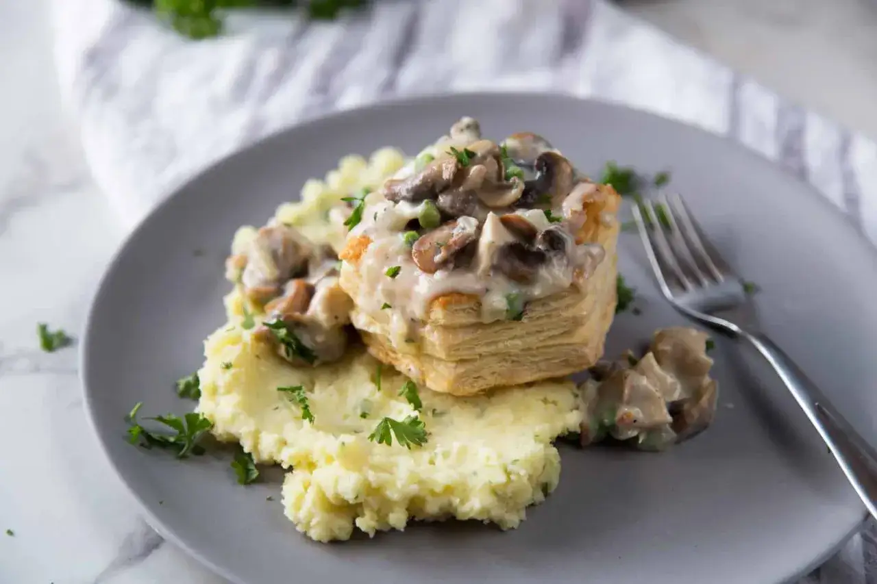 Un vol-au-vent garni d'une sauce crémeuse au poulet et aux champignons, servi avec une purée de pommes de terre et du persil frais.