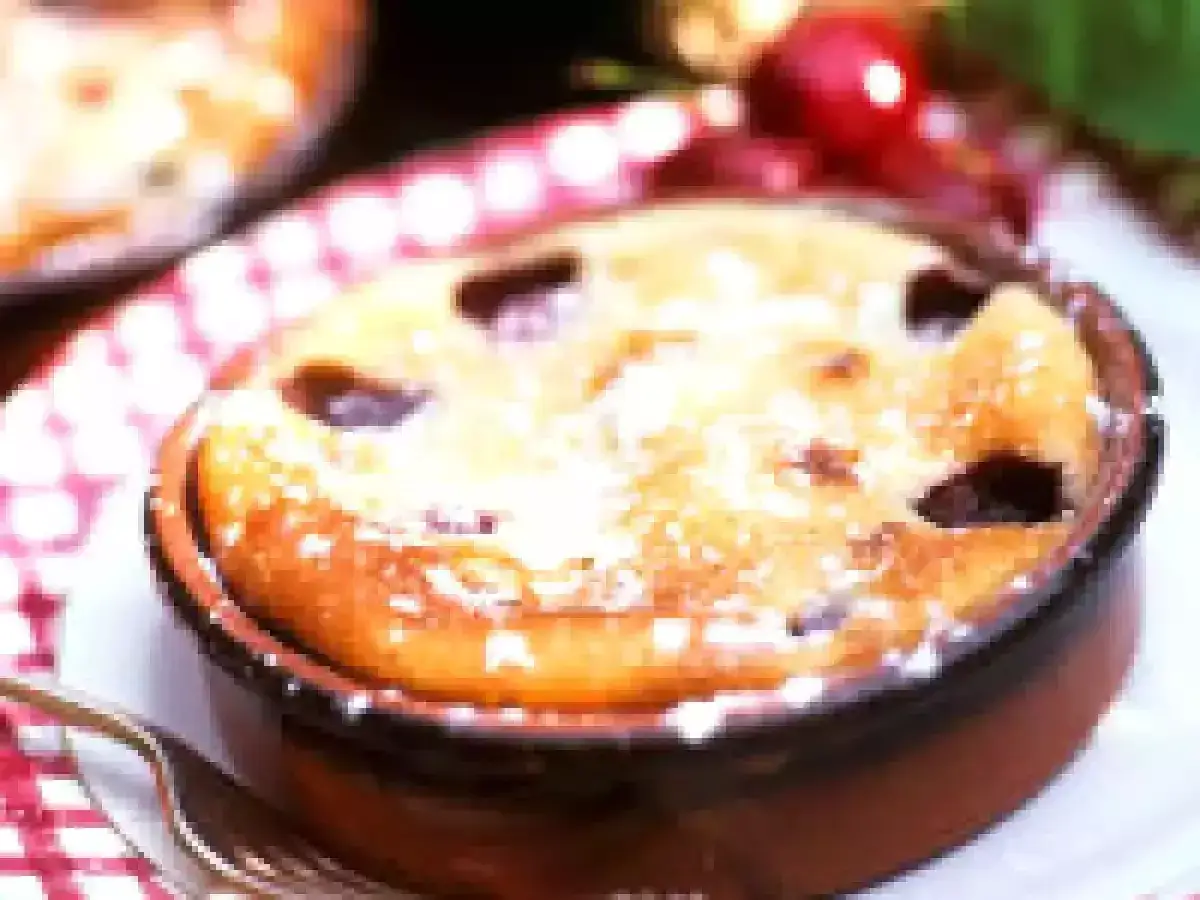 Un délicieux clafoutis aux prunes, saupoudré de sucre glace, dans un ramequin en terre cuite.