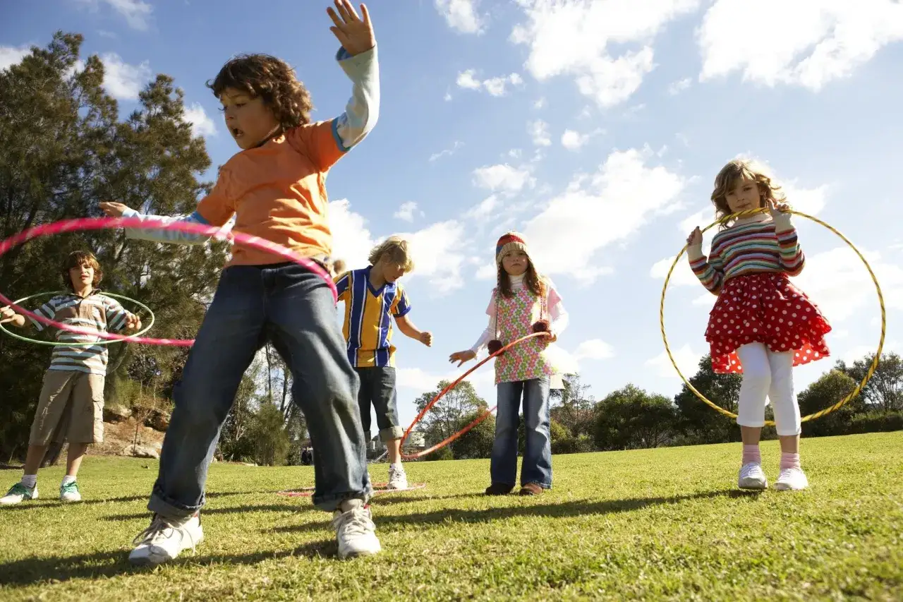 Niños de 6 a 12 años divirtiéndose con aros en un día soleado.