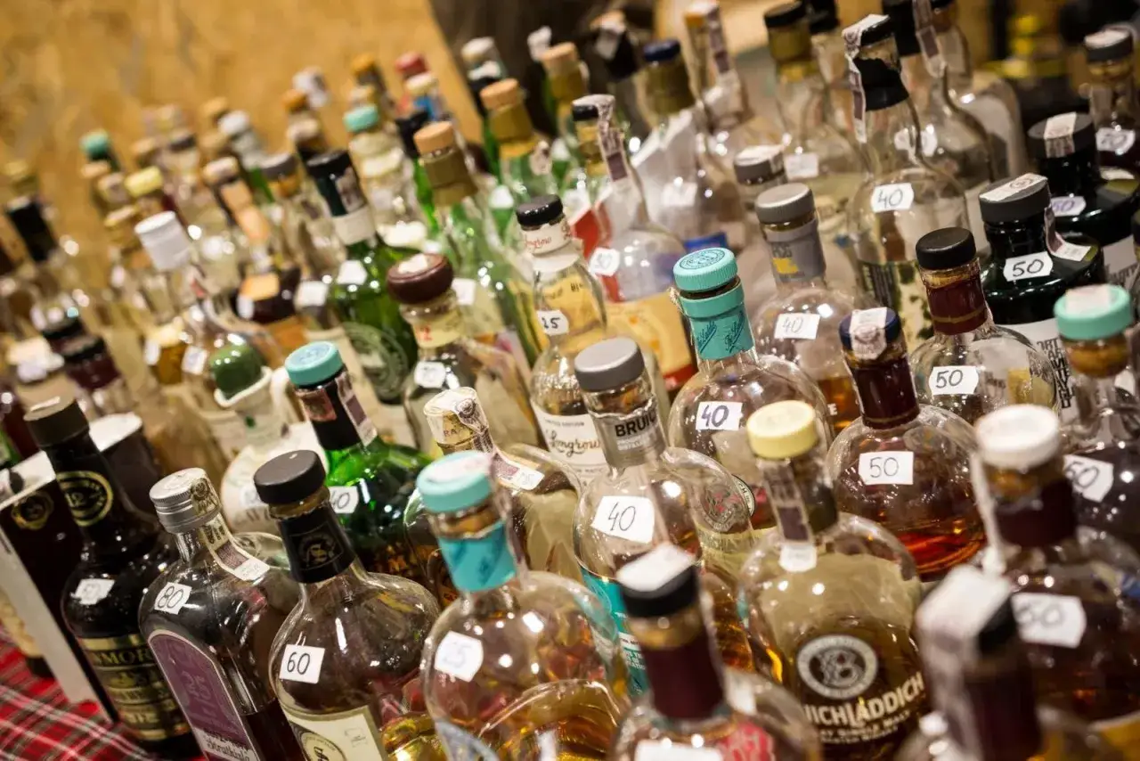 Mnóstwo butelek alkoholu, niektóre z etykietami cenowymi, gotowe do sprzedaży. Każda butelka to potencjalny dochód z akcyzy.