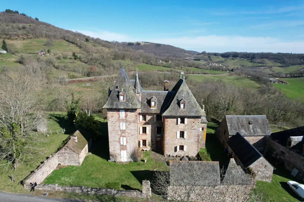 Vue aérienne d'un château abandonné, ses tours et ses dépendances se dressent au milieu d'une nature verdoyante et vallonnée.
