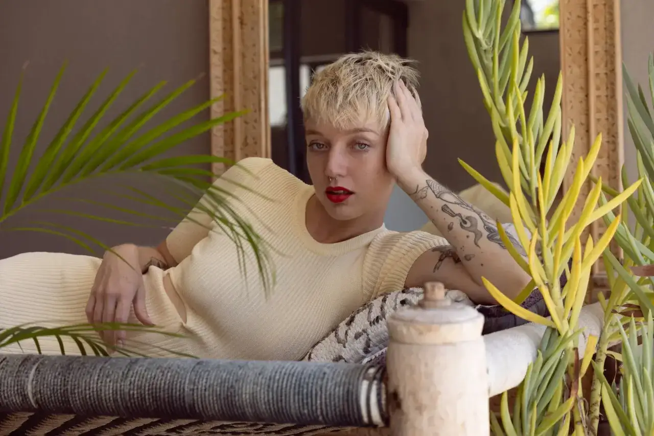Kobieta z tatuażami i krótkimi blond włosami, w kremowej sukience, leży na kanapie. To inspiracja, jak zostać modelką Zary.