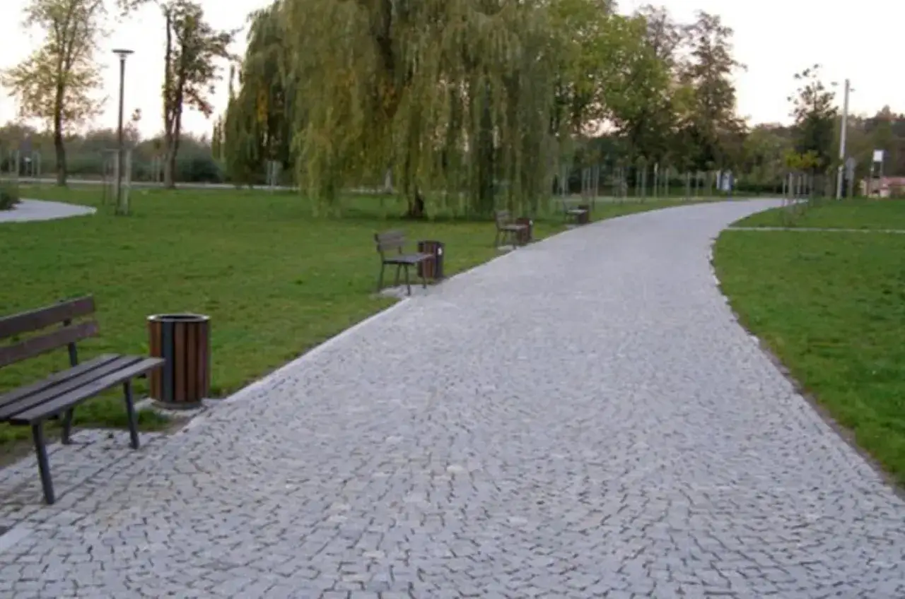Urokliwa ścieżka z kostki granitowej w parku, otoczona zielenią i drzewami.