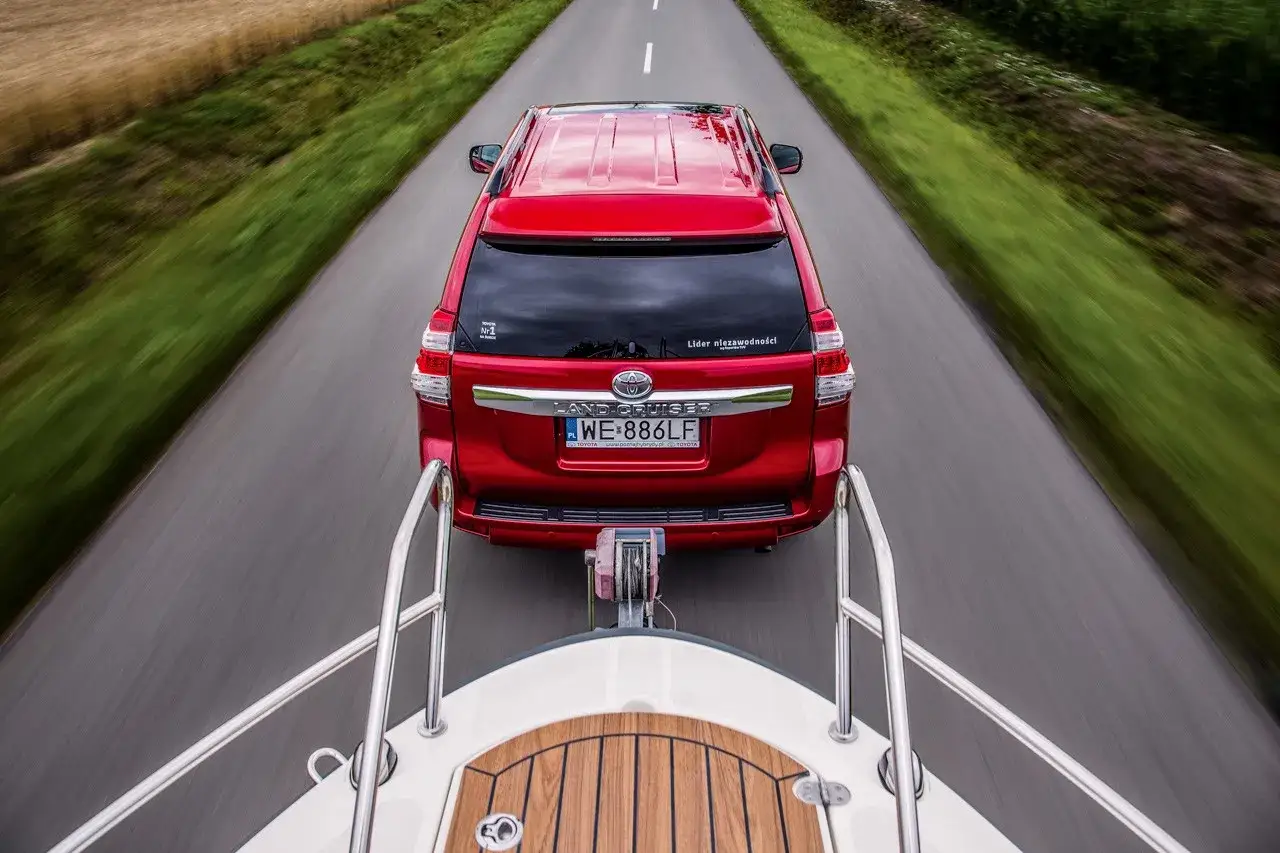 Czerwony Land Cruiser ciągnie łódź. Posiadanie prawa jazdy na przyczepę to klucz do takiej podróży.