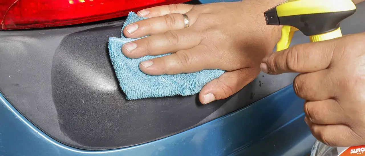 Dłoń z pierścionkiem aplikuje czernidło do plastików zewnętrznych na zderzak samochodu, przywracając mu głęboki kolor.