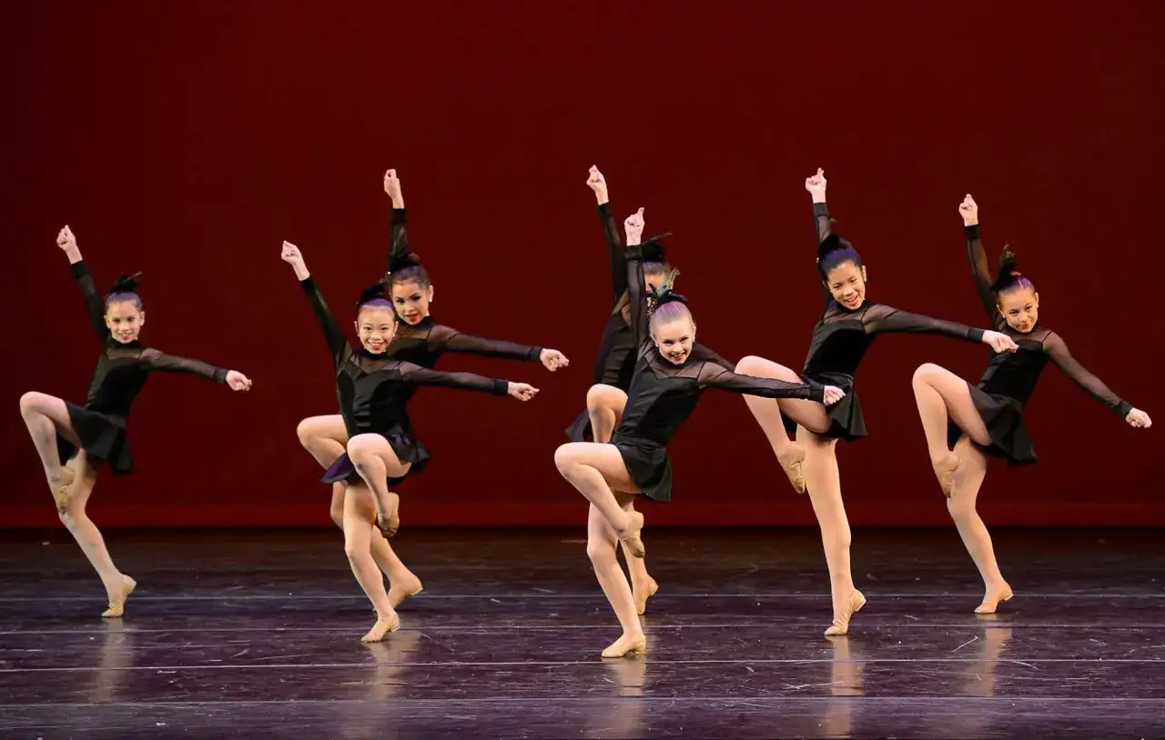 Bambine in un corso di danza eseguono una coreografia con grazia, indossando eleganti abiti neri.
