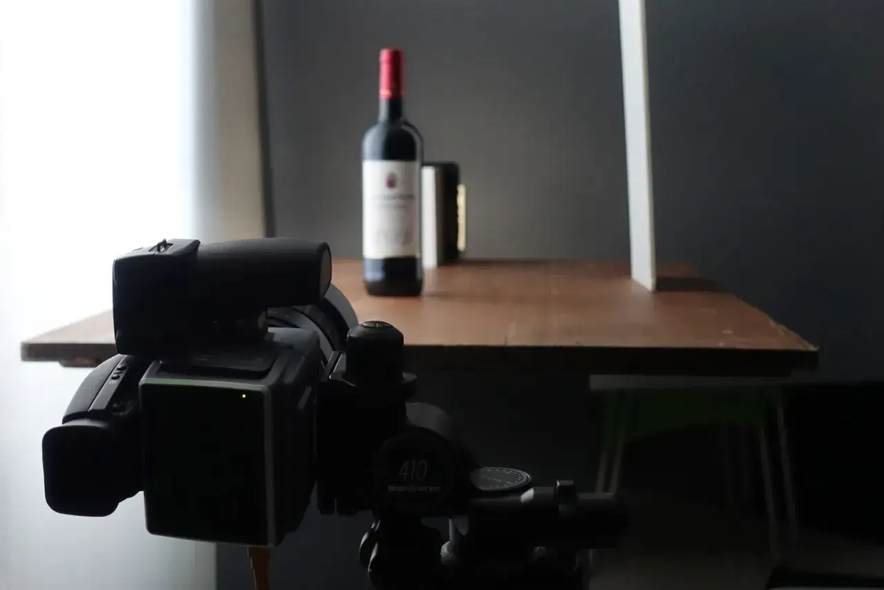 A bottle of wine is set up for natural product photography, with a camera on a tripod in the foreground.