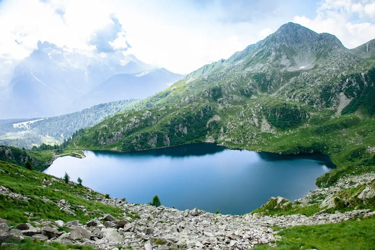 Lago alpino blu intenso circondato da montagne verdi e rocciose. Un luogo incantevole da scoprire a Madonna di Campiglio.