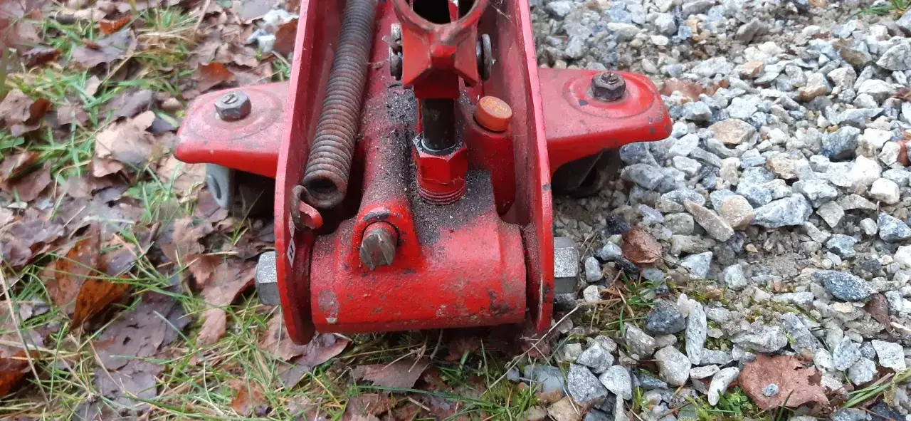 Detaljerad bild av en r&ouml;d domkraft. En fj&auml;der och en skruv syns tydligt. Kanske dags att fylla olja i domkraften f&ouml;r att den ska fungera som den ska.