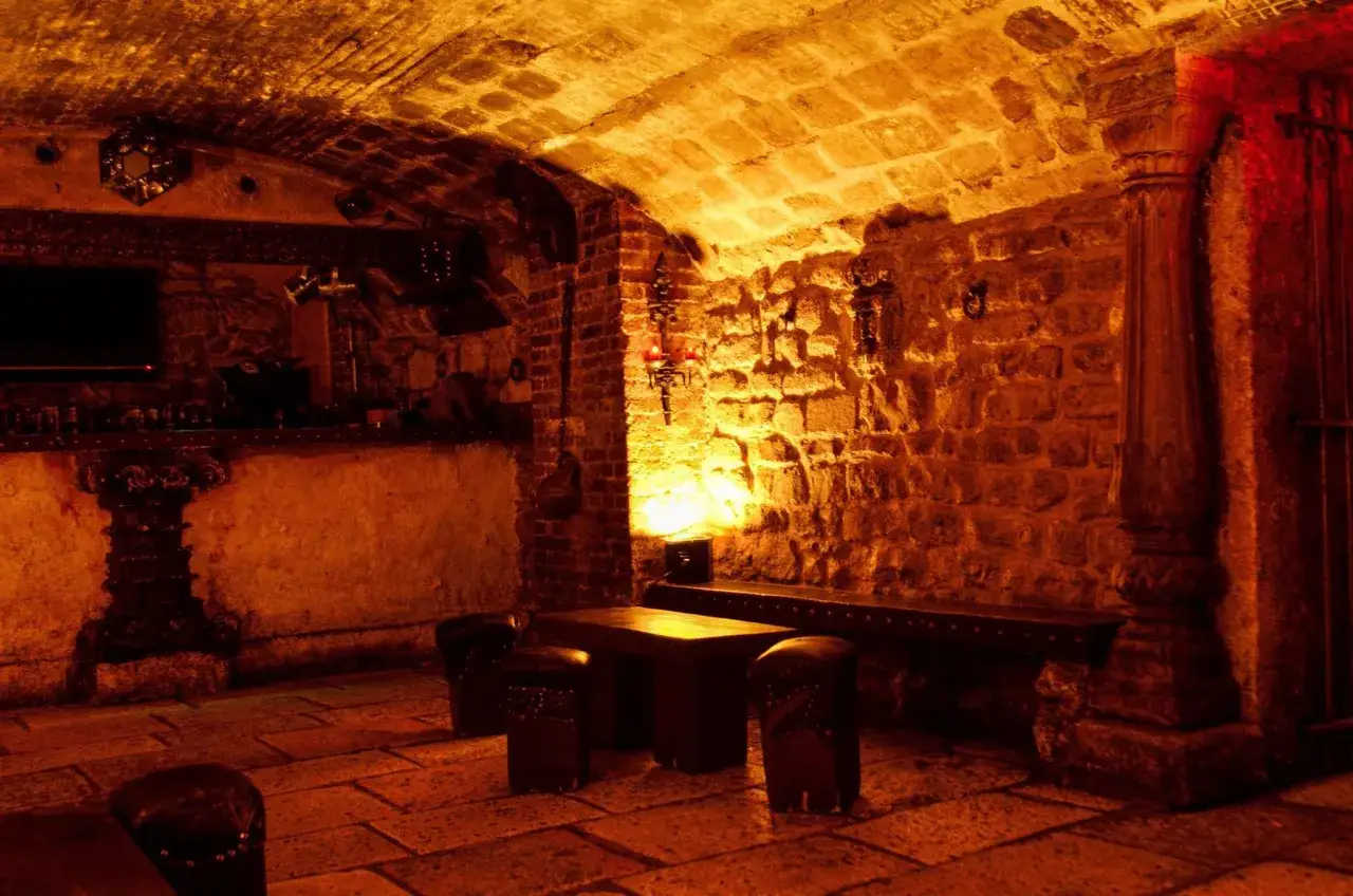 Ambiance chaleureuse dans une taverne médiévale parisienne. Pierres apparentes, voûtes, mobilier rustique et éclairage tamisé créent une atmosphère unique.