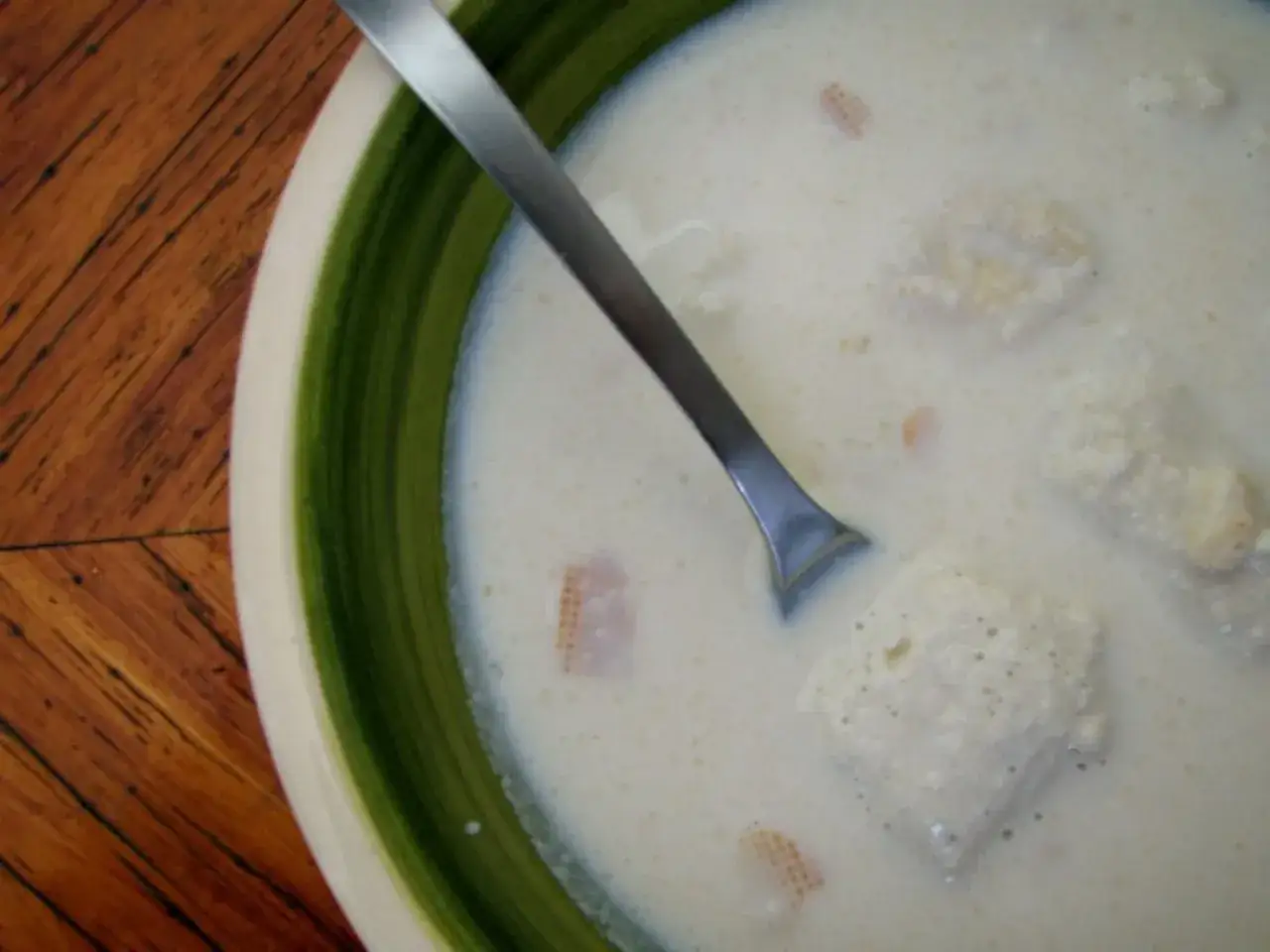 Un plato de sopa de almendras cremosa con trozos de pan y una cuchara plateada.