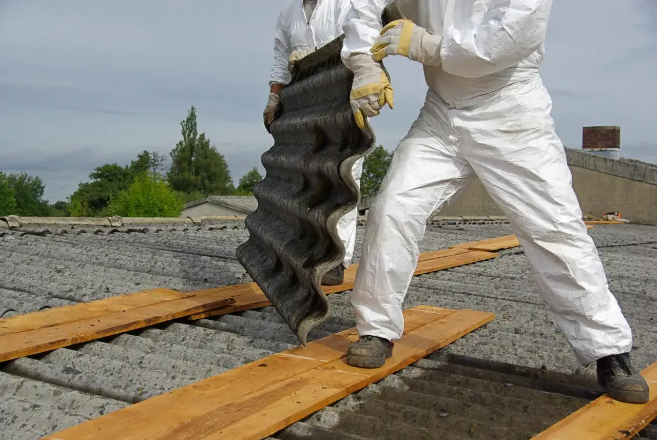 Osoby w kombinezonach ochronnych usuwają z dachu eternit, materiał zawierający azbest.