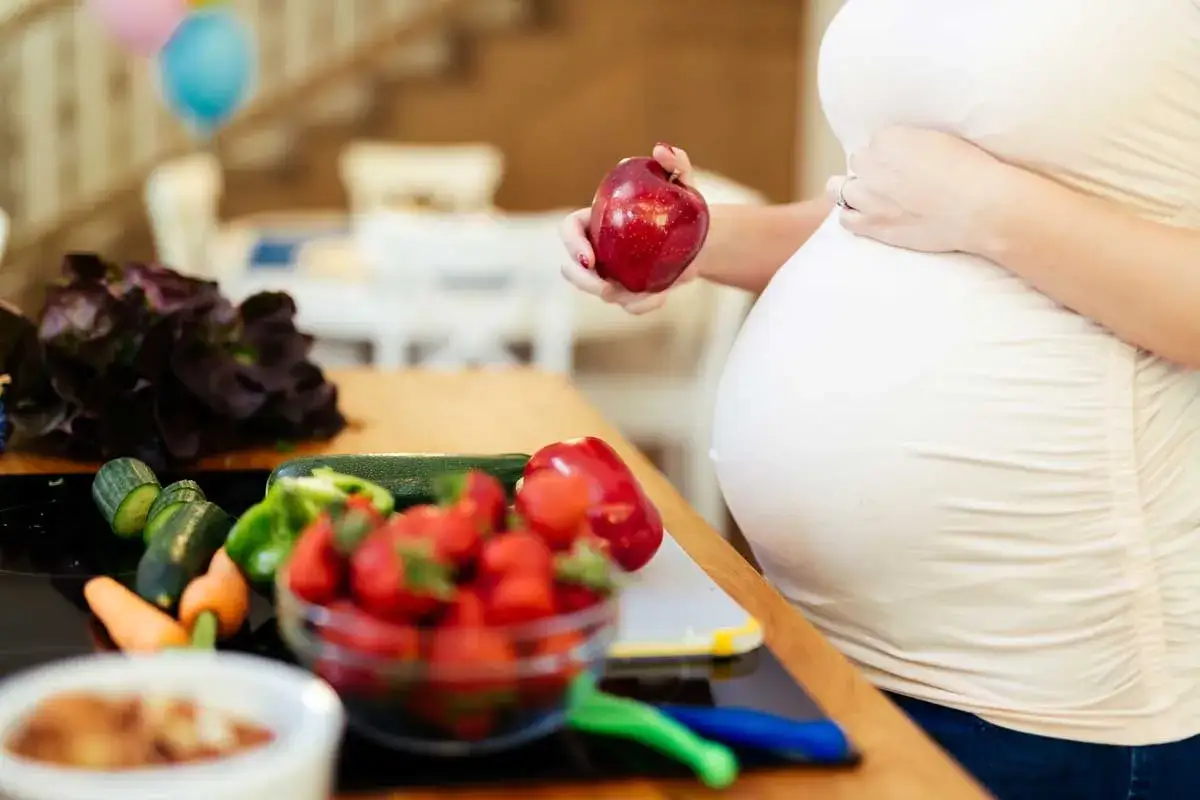 Schwanger mit Bauch und frischem Obst/Gem&uuml;se. Gesunde Ern&auml;hrung kann bei Durchfall in der Schwangerschaft helfen.