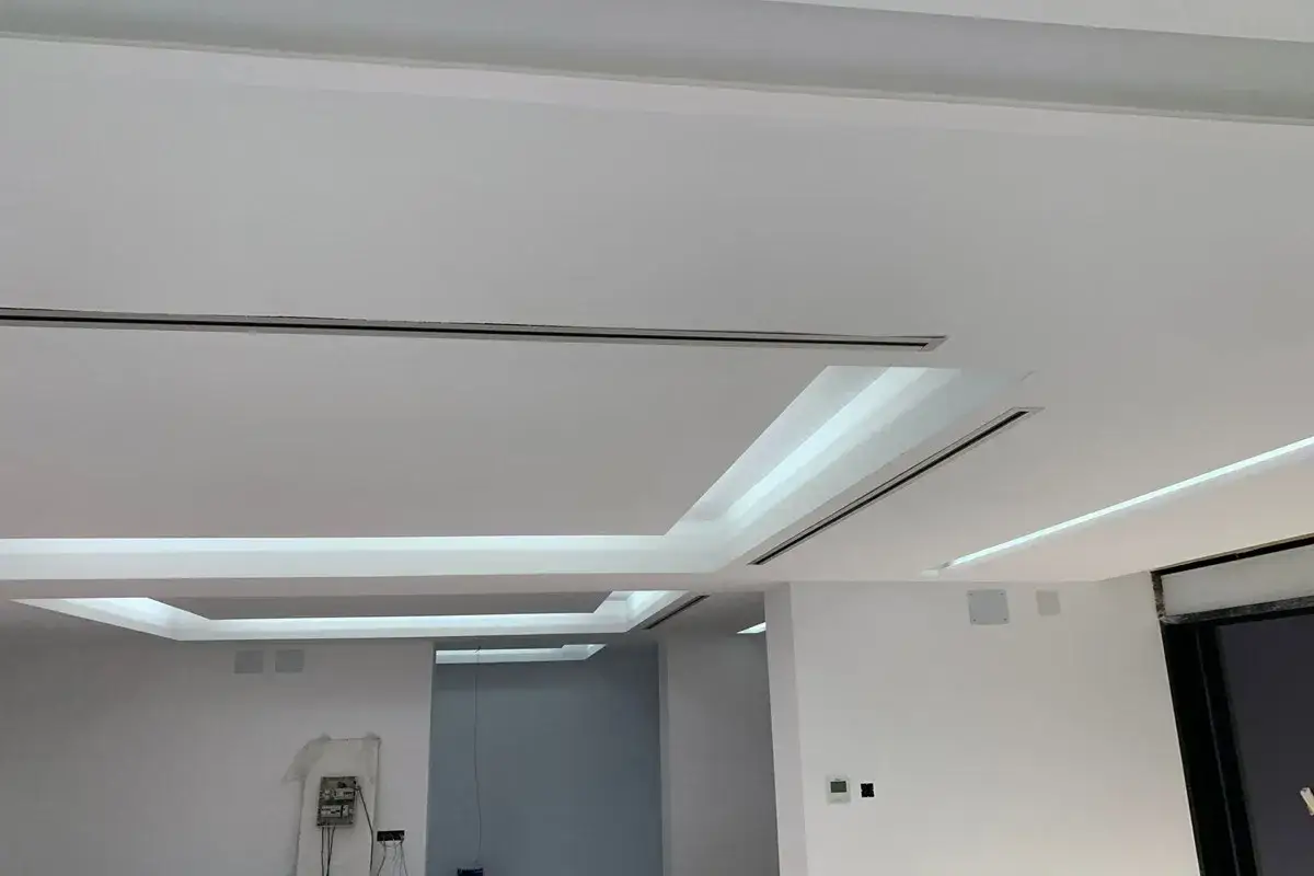 Falso techo moderno con iluminación integrada y conductos de aire acondicionado ocultos, creando un ambiente limpio y minimalista.