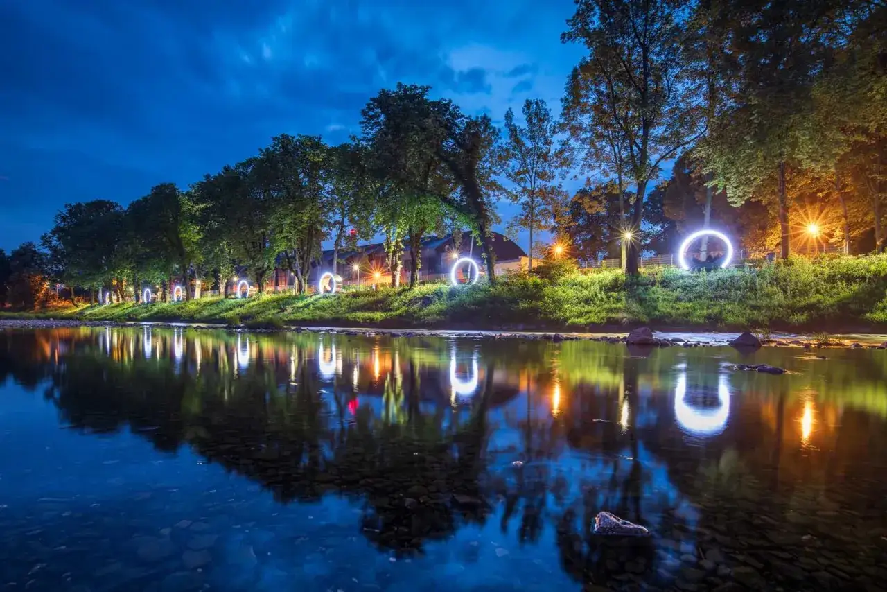 Rzeka płynie przez Cieszyn, odbijając świetlne kręgi i drzewa. Nocne iluminacje tworzą magiczny klimat.