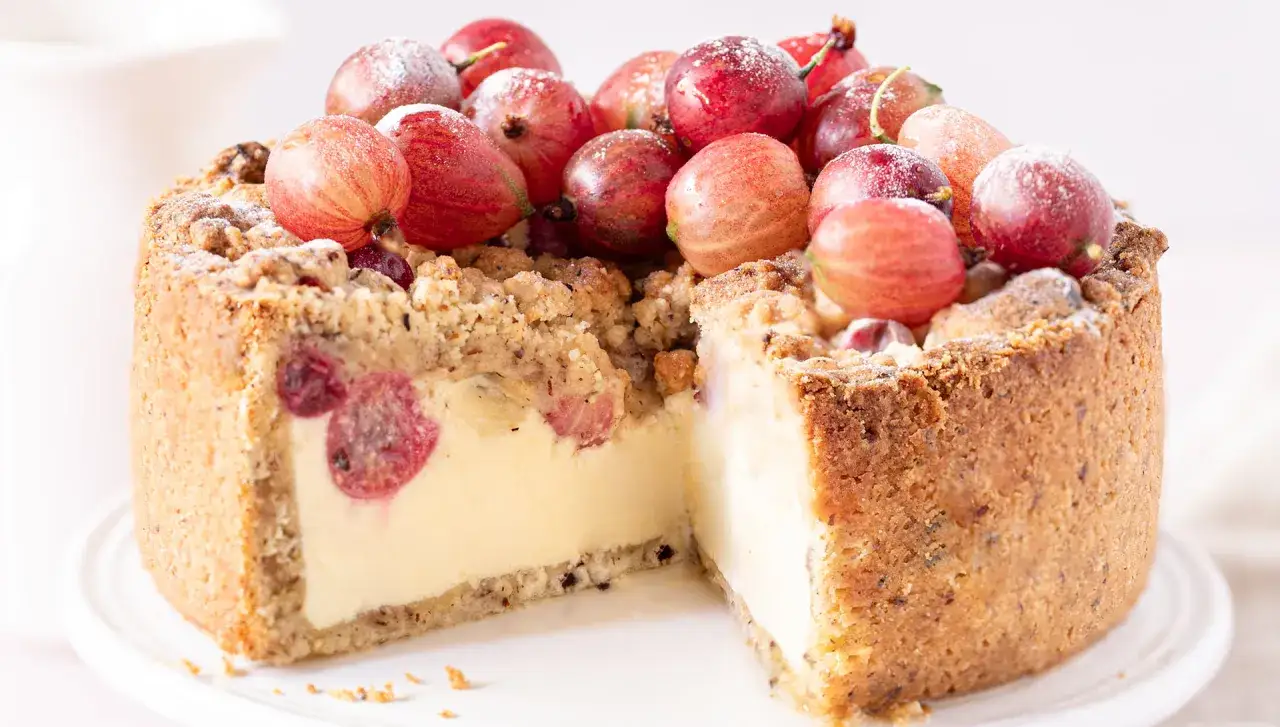 Ein saftiger Stachelbeerkuchen mit knusprigen Streuseln und frischen Stachelbeeren obendrauf, bestäubt mit Puderzucker.