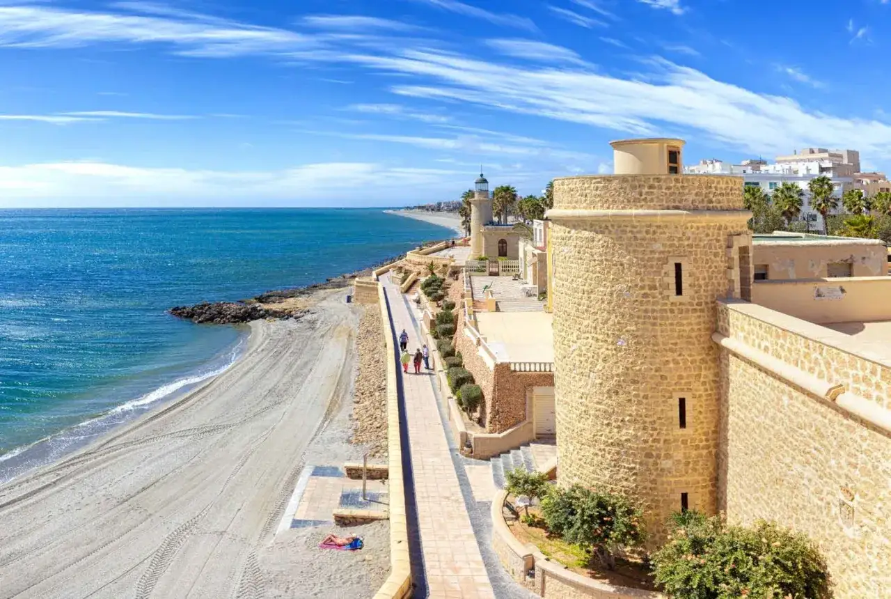 Paseo junto al mar en Roquetas de Mar, Almería. Una torre vigía de piedra, un faro y la playa invitan a disfrutar del sol y el Mediterráneo.