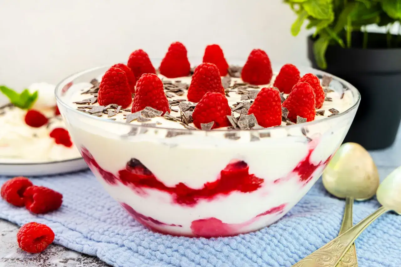 Himbeer Baiser Nachtisch in einer Glasschüssel, garniert mit frischen Himbeeren und Schokostückchen. Ein köstlicher Genuss!