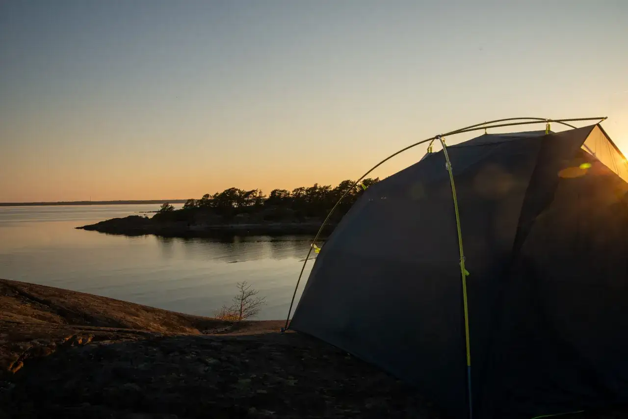 En tältplats vid vattnet, perfekt för att campa i Stockholm. Solnedgången färgar himlen gyllene över skärgården.
