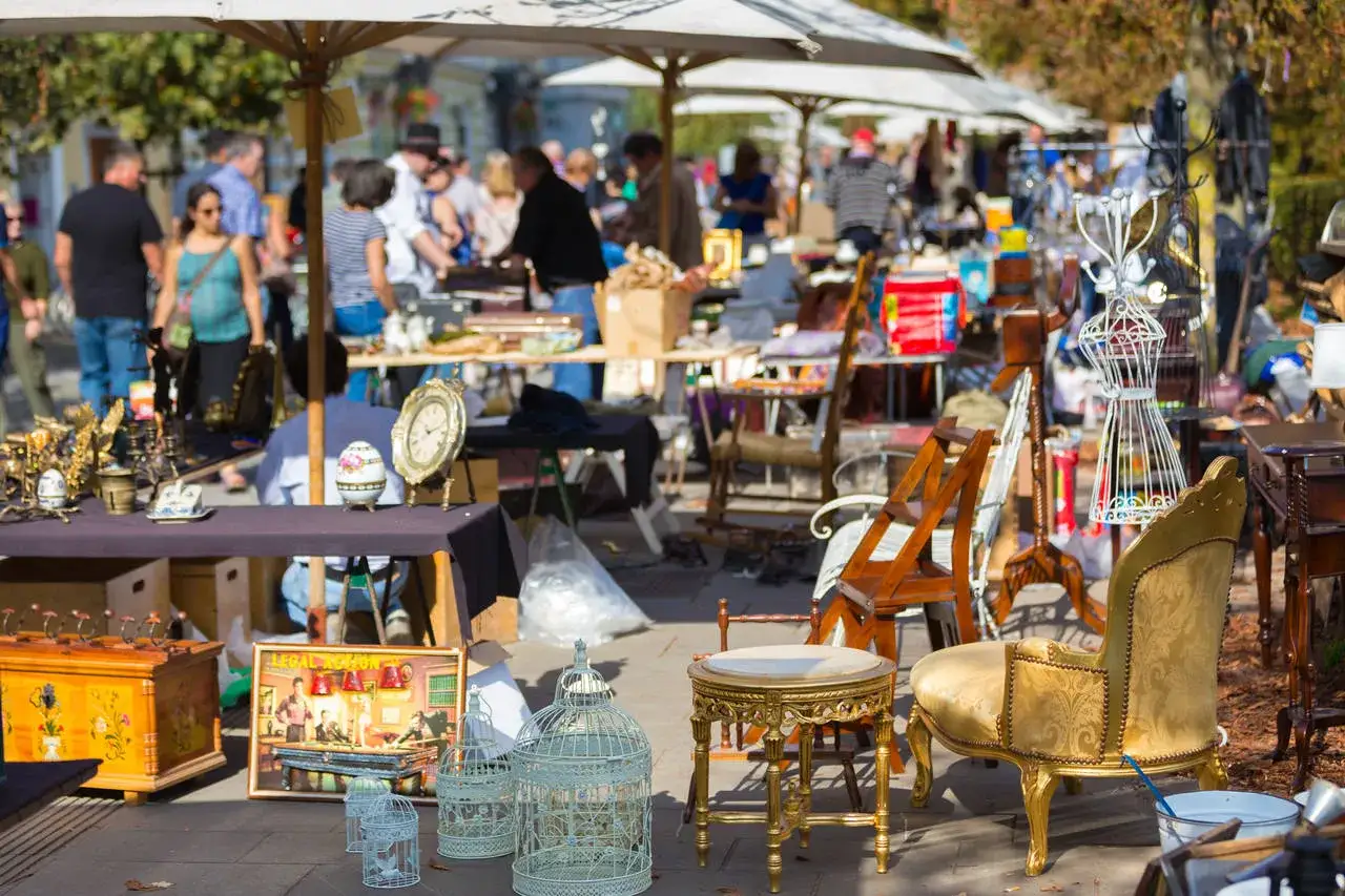 Buntes Treiben auf dem Flohmarkt mit vielen Sachen: antike Uhren, Vogelkäfige, Möbel und Bilder.