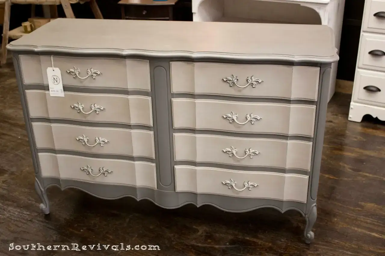 C&oacute;moda con **muebles pintados a la tiza en dos colores**, gris y beige, con tiradores ornamentados.