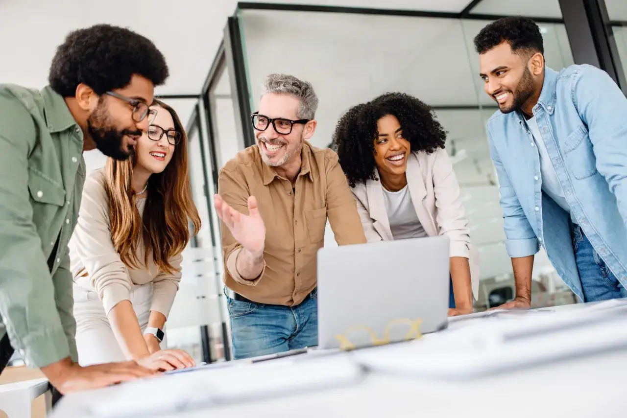 A diverse team collaborates, showcasing effective ai leadership as they discuss a project around a laptop.