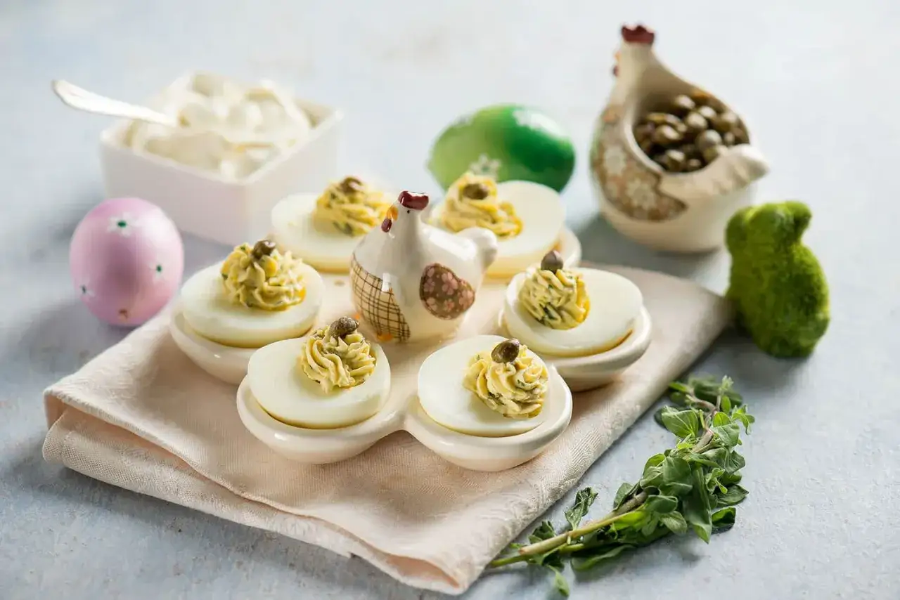 Uova ripiene vegetariane con ceci, guarnite con capperi e erbe aromatiche, su un piatto con decorazioni pasquali.