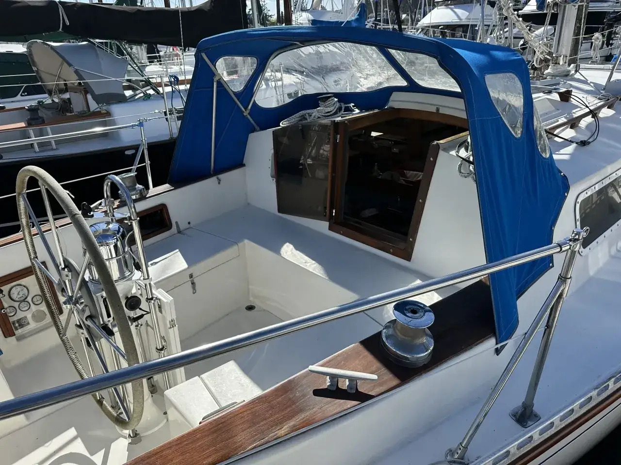 Cockpit d'un voilier d'occasion de 9-10 mètres, avec capote bleue, barre franche et winchs. Prêt pour de nouvelles aventures.