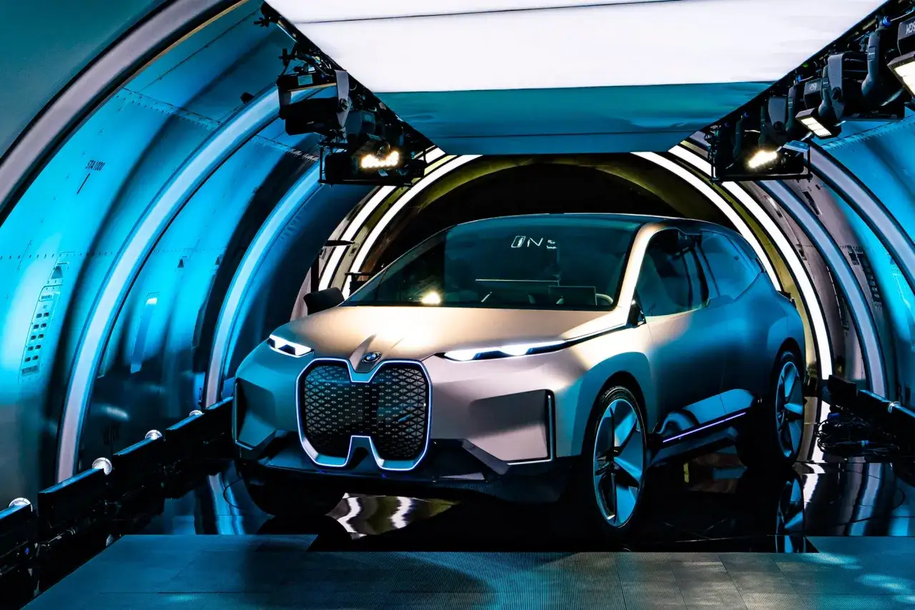 Nowe BMW iX w futurystycznym tunelu, z niebieskim podświetleniem i nowoczesnym designem.