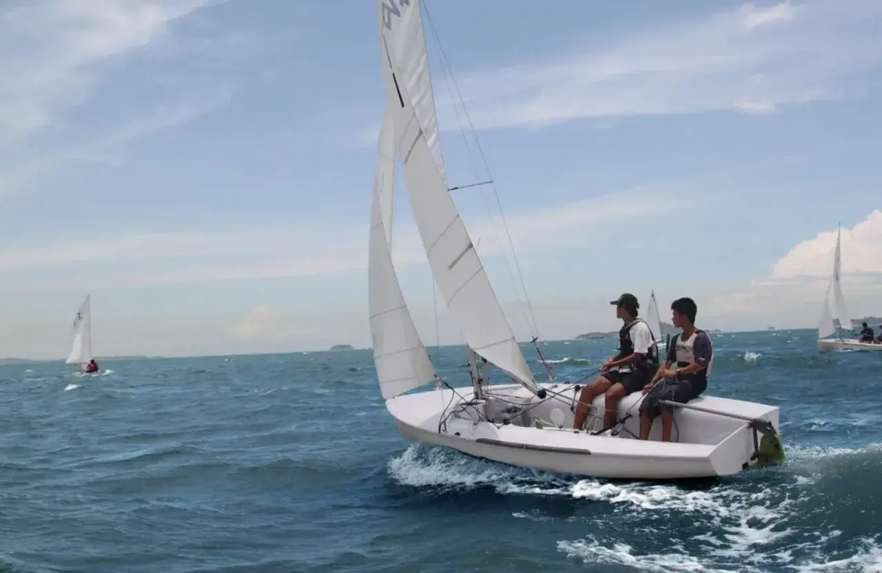 Deux jeunes hommes naviguent sur un dériveur 420 par une journée ensoleillée. L'eau bleue est agitée par le vent.