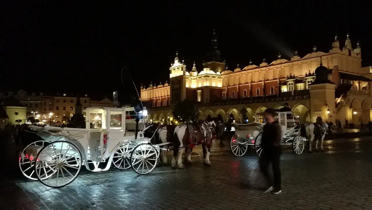 Kraków nocą: dorożki na Rynku Głównym, w tle Sukiennice. Idealne miejsce na wieczorne spacery, a potem do jednego z licznych klubów w Krakowie.
