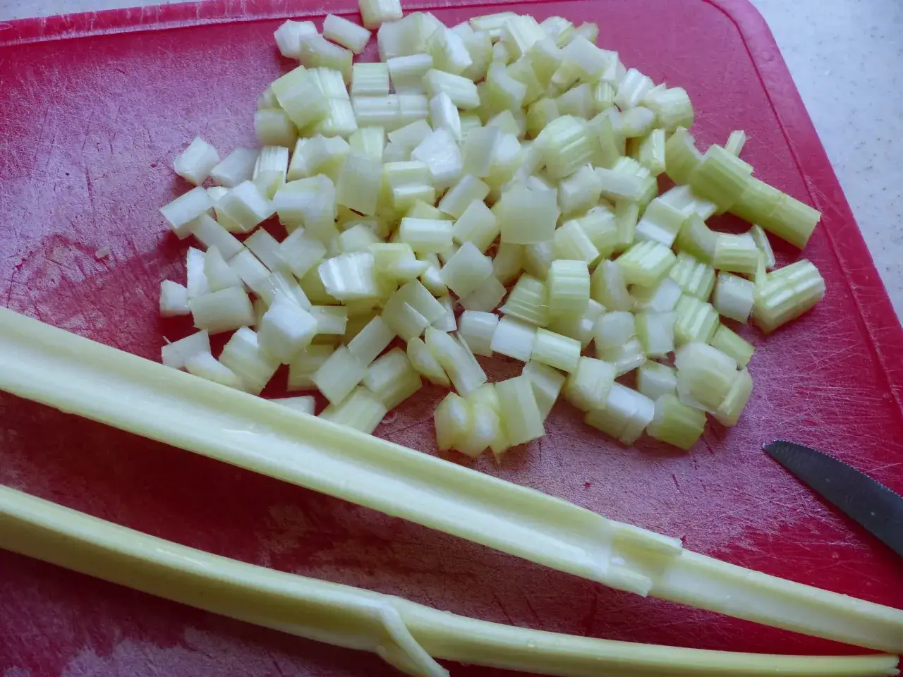 Céleri branche coupé en dés sur une planche rouge, prêt pour une recette.