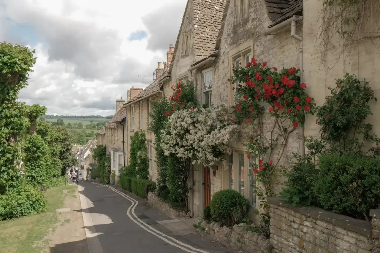 Kamienne domy w Cotswolds porośnięte kwitnącymi różami i bluszczem, malownicza uliczka z zielenią.