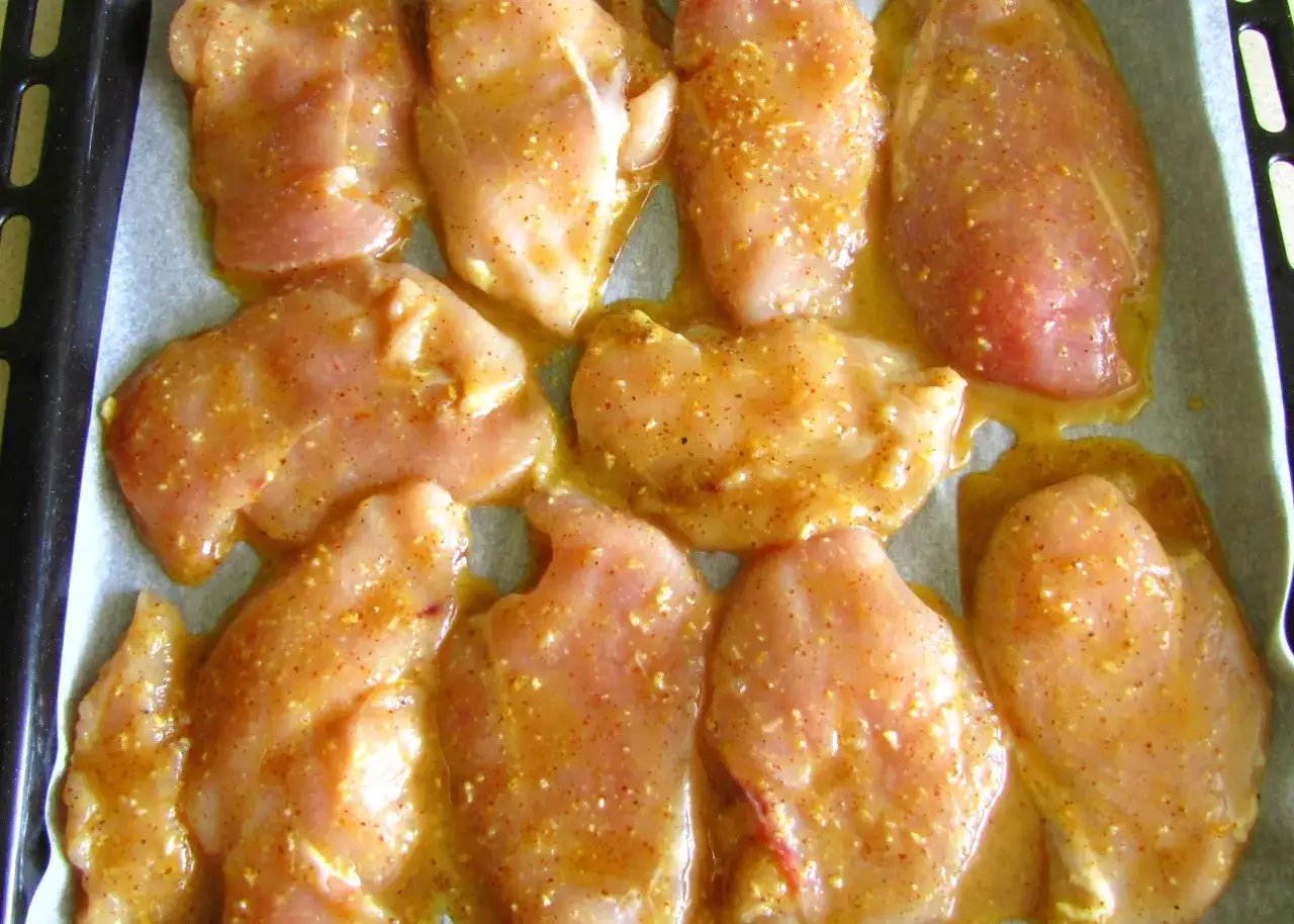 Surowe kawałki kurczaka w miodzie i musztardzie, gotowe do pieczenia.