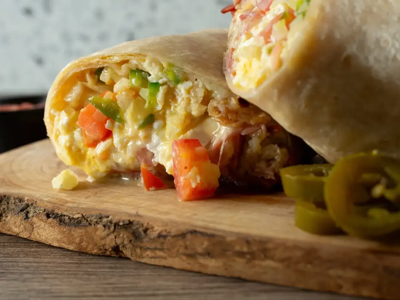 Pyszna tortilla z jajecznicą, pomidorami i papryką, podana na drewnianej desce z plasterkami jalapeno.