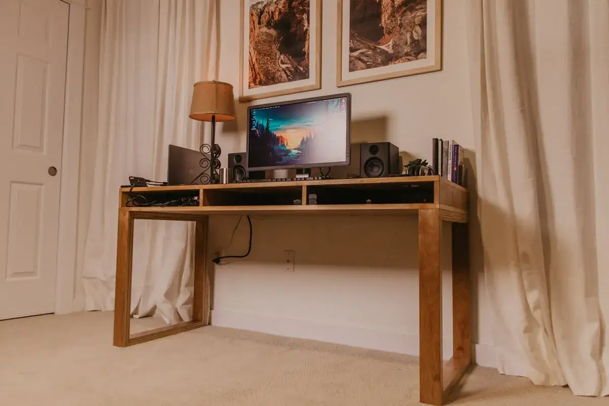 Un bureau DIY en bois clair, avec un écran d'ordinateur, des enceintes, une lampe et des livres.
