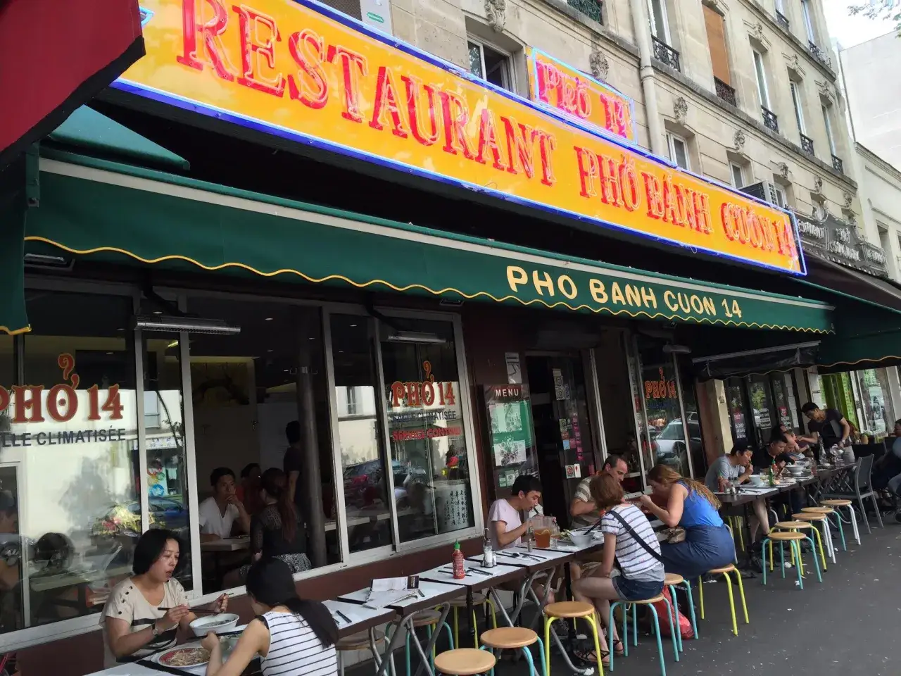Restaurant Pho 14, une enseigne lumineuse promet le meilleur pho. Des clients savourent ce plat réconfortant en terrasse.