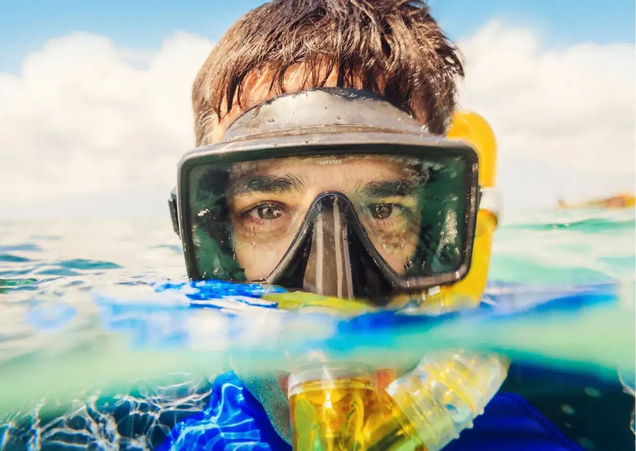 Mężczyzna w masce do snorkelingu, z rurką w ustach, pokazuje, jak działa maska do snorkelingu, pozwalając oddychać pod wodą.