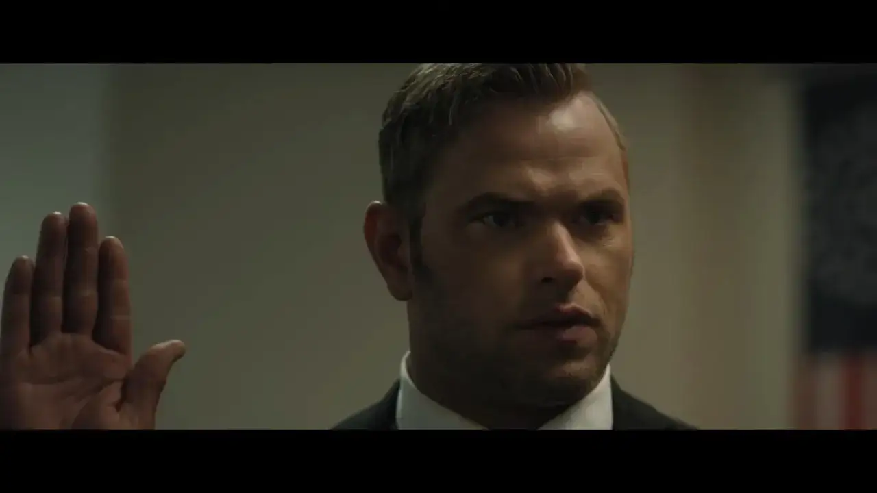 Cam Gigandet med upph&ouml;jd hand, sv&auml;r en ed framf&ouml;r en amerikansk flagga.