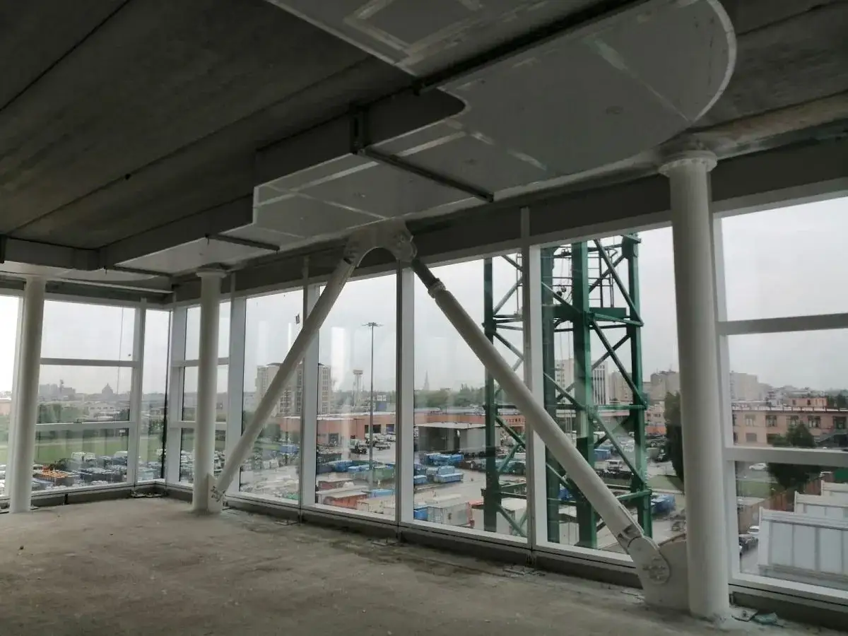 Struttura interna con pilastri bianchi e travi metalliche, protette da vernice intumescente. Vetrate ampie con vista su un paesaggio urbano industriale.