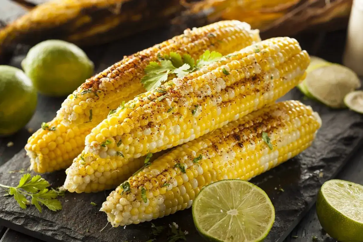 Pannocchie cotte alla griglia, condite con spezie e prezzemolo, servite con spicchi di lime. Un modo gustoso per imparare come cucinare le pannocchie.