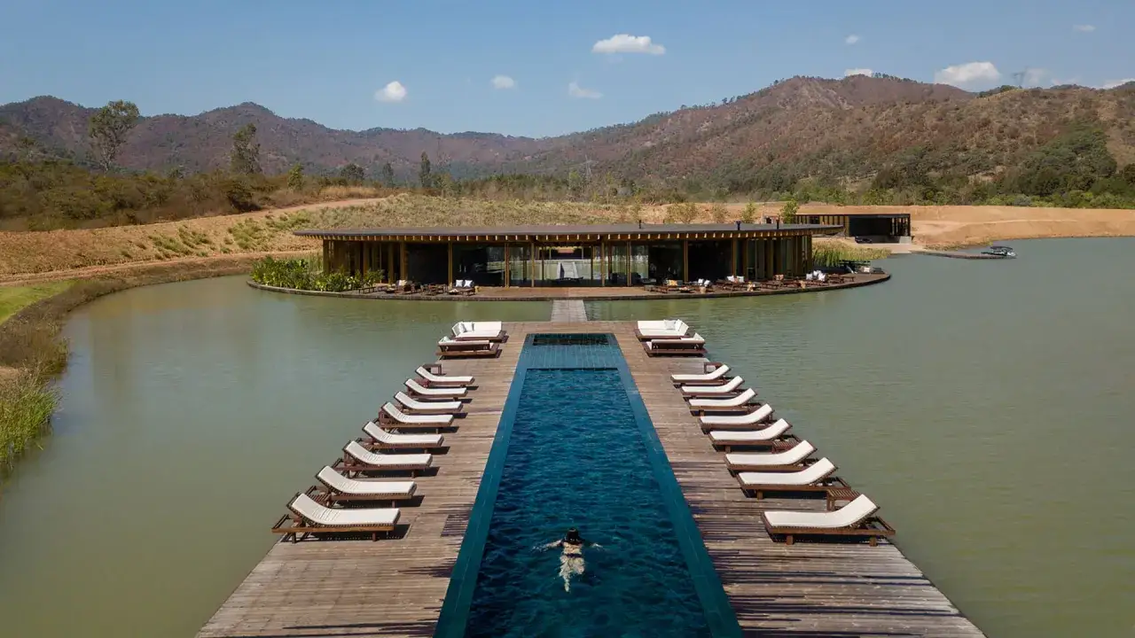 Un homme nage dans une piscine à débordement, un exemple de comment faire un lac artificiel avec un ponton et un bâtiment moderne.