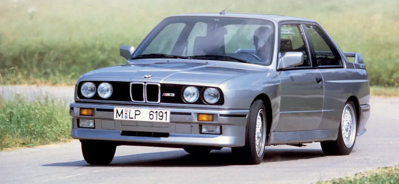 Silberner BMW E30 M3, Baujahr 1986, f&auml;hrt auf einer Landstra&szlig;e.