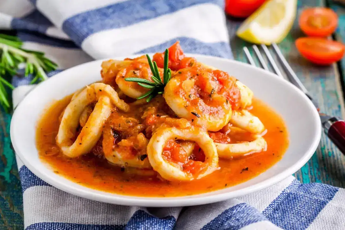 Calamari in umido, teneri anelli di calamaro cotti in un sugo rosso saporito, guarniti con rosmarino fresco.