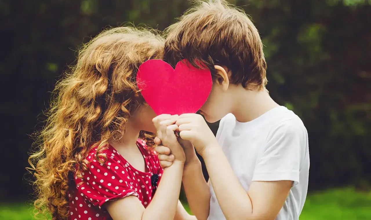 Zwei Kinder halten ein rotes Herz, das ihre Gesichter verdeckt. Ein zarter Moment, der die Anfänge der psychosexuellen Entwicklung symbolisiert.