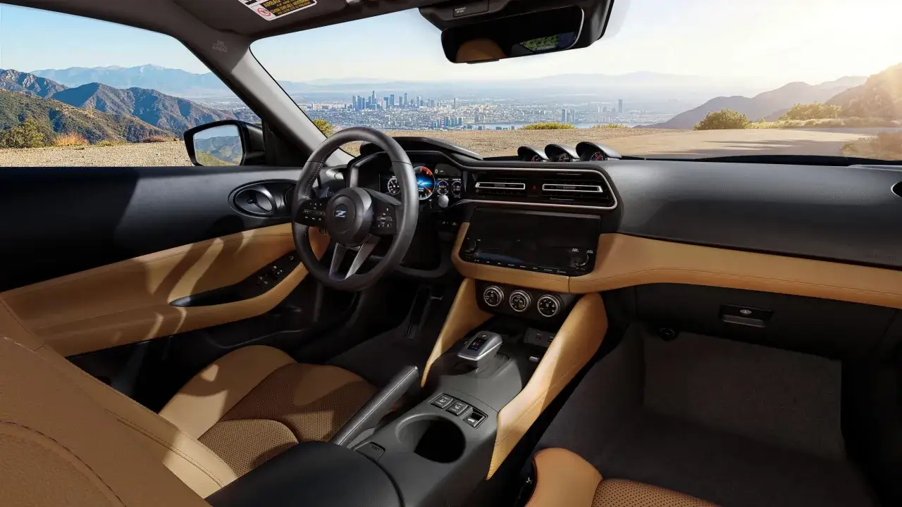 Interiör i en Nissan 400Z med lädersäten i brunt och svart, en modern instrumentpanel och en vidsträckt utsikt över en stad och berg.