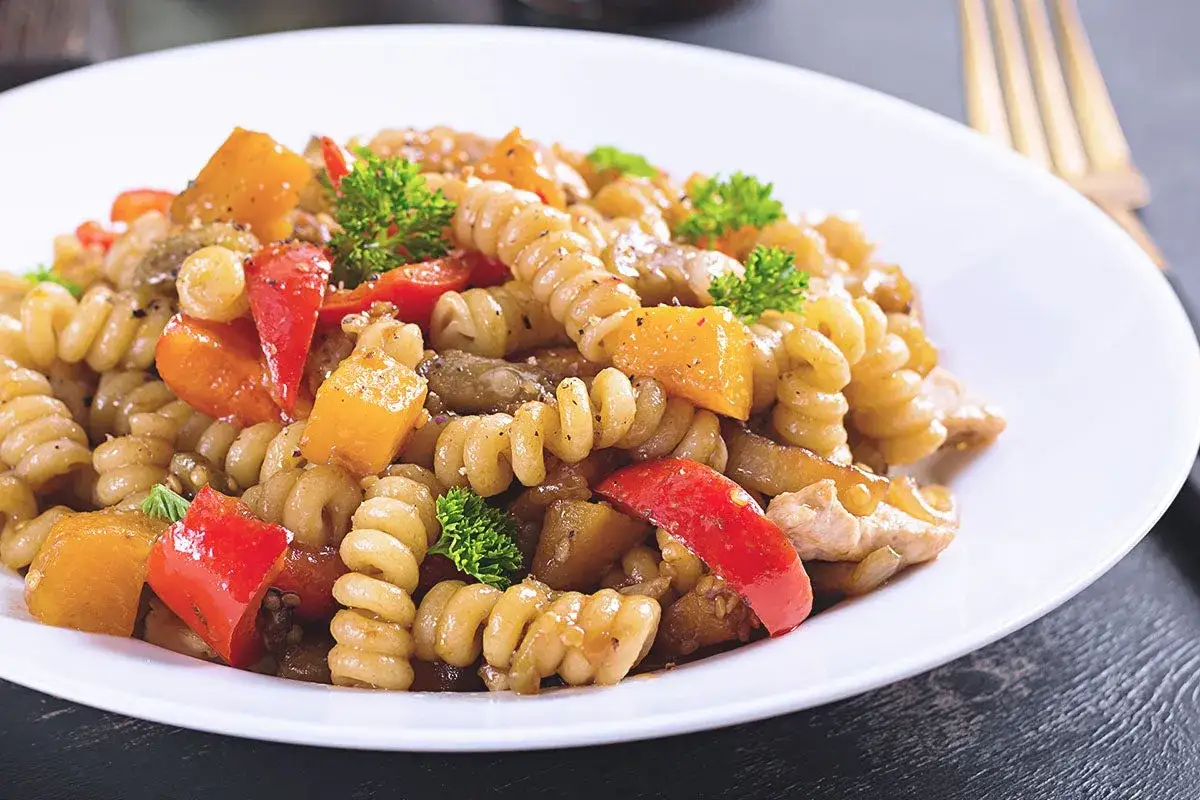 Fusilli con peperoni rossi e gialli, zucchine e pollo, guarniti con prezzemolo fresco. Un piatto colorato e saporito.